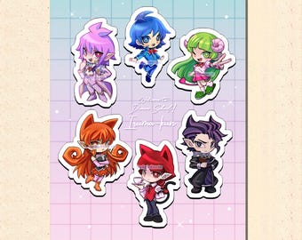 Puede incluir: Una hoja de pegatinas con seis personajes de estilo anime en colores vibrantes. Los personajes tienen peinados y atuendos únicos, con una mezcla de tonos rosa, azul, verde, naranja y morado. El texto "Welcome! Demon School! Iruma-kun" también es visible.