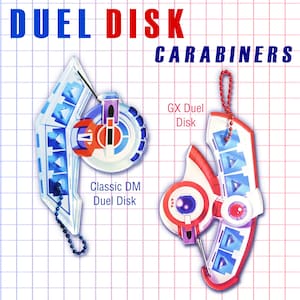 Puede incluir: Dos mosquetones Duel Disk, uno etiquetado como "Classic DM Duel Disk" y el otro como "GX Duel Disk". Los mosquetones son blancos, rojos y azules, con enganches de cadena. El texto "DUEL DISK CARABINERS" está en la parte superior.