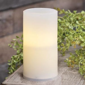 May include: A white frosted glass candle with a warm white LED light inside. The candle is sitting on a wooden surface.