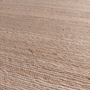 May include: Close-up of a natural fiber rug with a woven texture. The rug is a light brown color and has a subtle sheen.