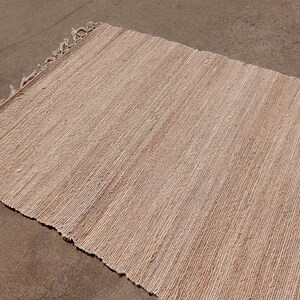May include: A natural fiber rug with a woven texture in a light beige color. The rug has frayed edges.