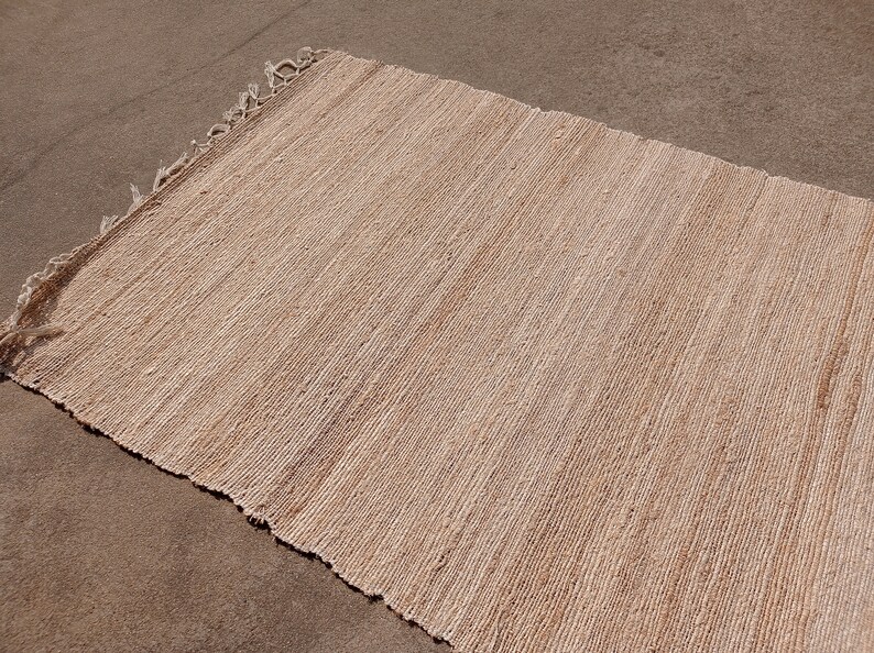 May include: A natural fiber rug with a woven texture in a light beige color. The rug has frayed edges.