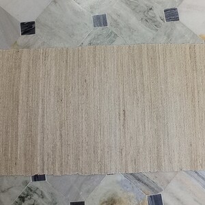 May include: A natural fiber rug with a woven texture. The rug is light brown and has a frayed edge.