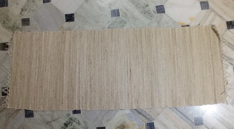 May include: A natural fiber rug with a woven texture. The rug is light brown and has a frayed edge.