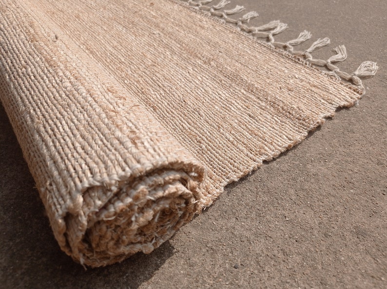 May include: A rolled-up natural fiber rug with fringed edges. The rug is a light beige color and has a woven texture.