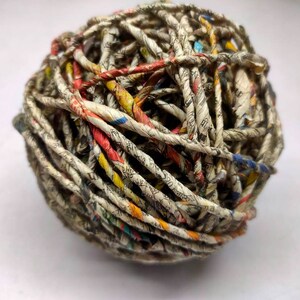 May include: A ball of twine made from recycled paper. The twine is a mix of white, brown, yellow, red, and blue.