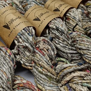 May include: Close-up of several spools of colourful recycled paper yarn. The yarn is made from shredded newspaper and other paper products. Each spool is labelled with the brand name "Silkeroute Art & Crafts Store".