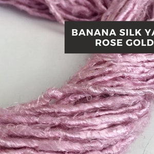 Puede incluir: Primer plano de un suave hilo de seda de pl&aacute;tano de color rosa dorado. El hilo est&aacute; enrollado holgadamente en un c&iacute;rculo, mostrando su textura y brillo.