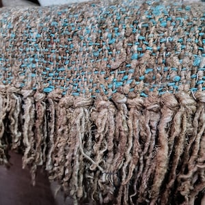Peut inclure: Gros plan sur un textile tissé marron et turquoise. Le tissu a un aspect texturé avec une frange sur le bord inférieur. Des accents turquoise sont tissés dans le matériau marron.