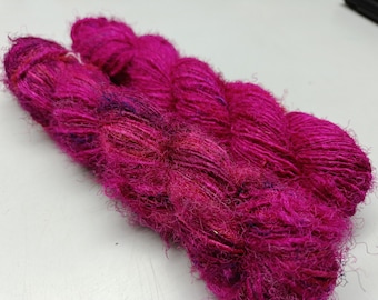 May include: Three skeins of magenta yarn with a fuzzy texture. The yarn is made of silk and wool.
