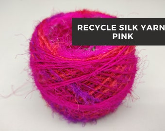 May include: A vibrant ball of pink recycled silk yarn. The yarn is a mix of bright pink, fuchsia, and orange hues, with a slightly fuzzy texture. Text on the image reads: RECYCLE SILK YARN-PINK.