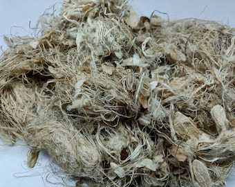 Könnte beinhalten: Nahaufnahme eines Haufens natürlicher Fasern, wahrscheinlich Leinen oder Hanf, in hellbrauner und weißer Farbe. Die Fasern sind verheddert und locker, mit einigen kleinen Teilen der Samenkapseln der Pflanze sichtbar.