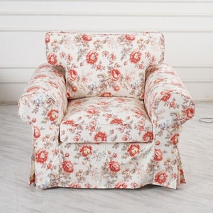 May include: A white armchair with a floral pattern in shades of red and pink. The armchair has a high back and a wide seat.