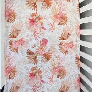 May include: A white fitted cot sheet with a floral pattern featuring pink and brown flowers and leaves. The sheet has the word "Palm" printed in the bottom right corner.