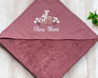 May include: A dusty rose hooded baby towel. The hood features an embroidered design of two deer with white flowers and the name "Clara Marie" in white script. The towel is made of a soft, plush material.