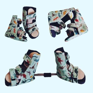 May include: A pair of green and black orthopaedic boots with dinosaur print fabric. The boots are connected by a metal bar.