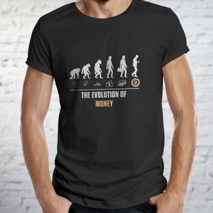 Può includere: Maglietta nera con una grafica che rappresenta l'evoluzione del denaro, con figure stilizzate che rappresentano diverse fasi della moneta, dal baratto al Bitcoin. Il testo "THE EVOLUTION OF MONEY" è stampato sotto la grafica.