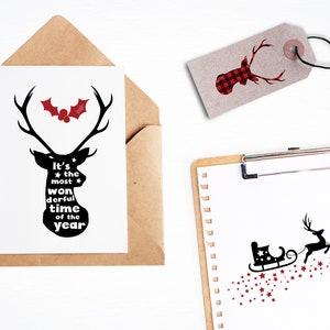 May include: A black and white silhouette of a reindeer with the text "It's the most wonderful time of the year" inside the silhouette. A red holly berry with green leaves is above the reindeer. The image is on a white card with a brown envelope.