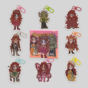 Peut inclure: Plusieurs porte-clés de personnages de dessins animés avec divers designs, dont un bouffon, une fée et un guerrier. Les porte-clés sont attachés à des fermoirs colorés. Une boîte rose avec le texte "Chappell Roan BLIND BOX" est au centre.