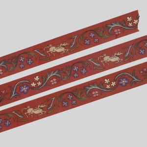May include: Three strips of red decorative tape featuring a repeating pattern of cream-colored unicorns, dark green scrolling foliage, and small clusters of purple and pink flowers. The design is printed in a continuous, flat, and linear format.