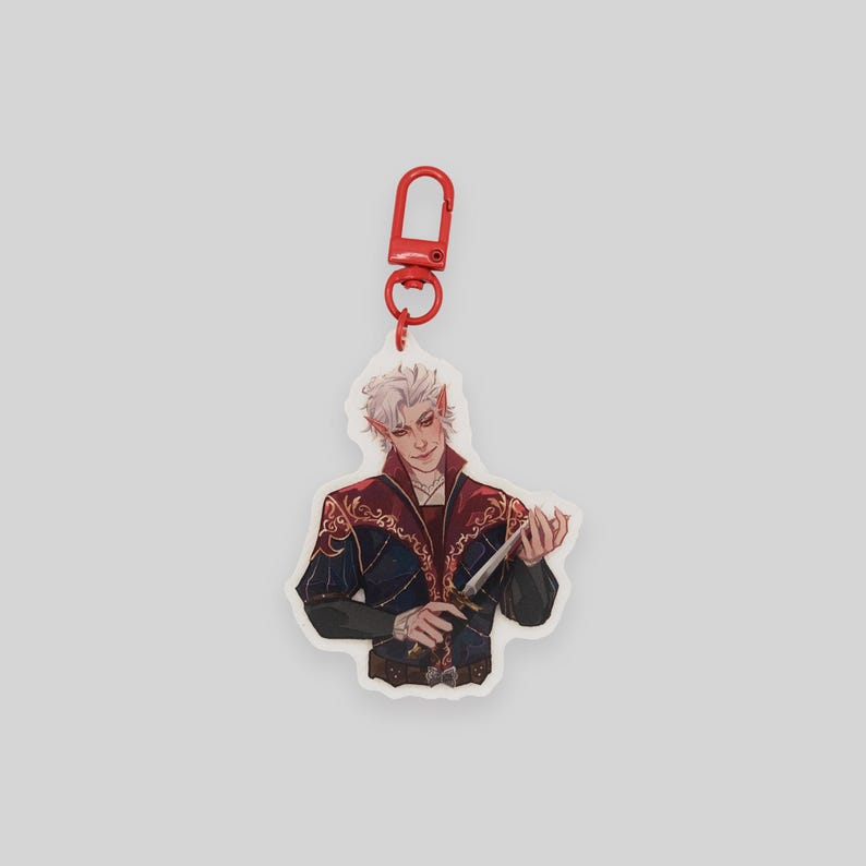 May include: A white acrylic keychain featuring a character with white hair, wearing a dark blue and red outfit with gold accents, holding a silver dagger. The keychain has a red metal clasp.