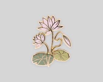May include: A gold-toned metal enamel pin featuring two light pink lotus flowers in bloom, one closed lotus bud, and two rounded green lily pads with dark green vein detailing, all outlined in thin gold metal lines against a plain background.