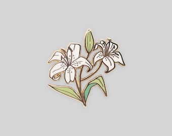 May include: A gold-toned metal enamel pin featuring two white lily flowers with dark brown outlines and detailing, accompanied by light green leaves and a single closed flower bud, all set against a plain, neutral background.