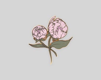 May include: A gold-toned metal enamel pin featuring two light pink peony flower buds with dark green leaves and stems. The design is outlined in thin gold metal lines, showcasing a layered petal structure for both flowers against a plain background.