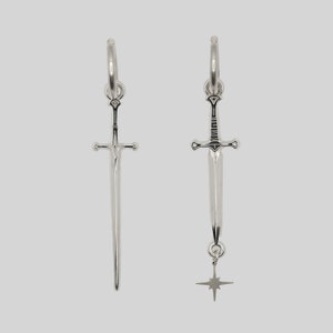 May include: A pair of silver hoop earrings with a sword charm. One earring has a star charm dangling from the sword.