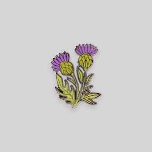 Pode incluir: Um alfinete de esmalte colorido com um design estilizado de cardo. O alfinete apresenta cabeças de flores roxas, botões amarelo-verdes e folhas verdes, todos delineados em prata. Este acessório floral é um item decorativo.