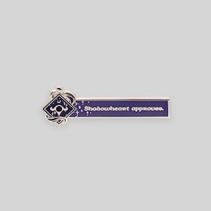 May include: A silver enamel pin with a purple background and a silver design. The pin features a stylized symbol with a crescent moon and a star, and the text "Shadowheart approves."