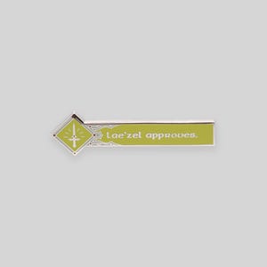 May include: A silver and green enamel pin with a diamond-shaped design featuring a sword and the text "Lae'zel approves."