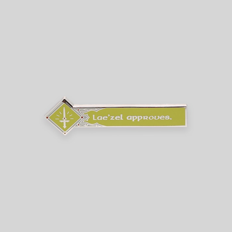May include: A silver and green enamel pin with a diamond-shaped design featuring a sword and the text "Lae'zel approves."