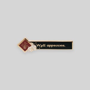 May include: Gold enamel pin with a red diamond shape featuring a stylized hand with a wand and the text "Wyll approves." The pin is on a white background.