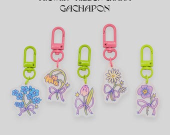 May include: Five flower and ribbon charm keychains with pink and green hardware. Each charm features a different floral design with a purple ribbon. The text "FLOWER + RIBBON CHARM GACHAPON" is at the top.