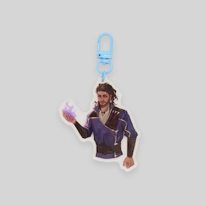 May include: A blue keychain with a clear acrylic charm featuring a cartoon illustration of a man with brown hair and a purple and blue outfit holding a purple flame in his hand.