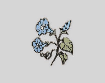 May include: A metal enamel pin featuring a botanical illustration of two light blue morning glory flowers with dark outlines. The design includes a slender dark stem, a single blue flower bud, and two light green heart-shaped leaves with veins.