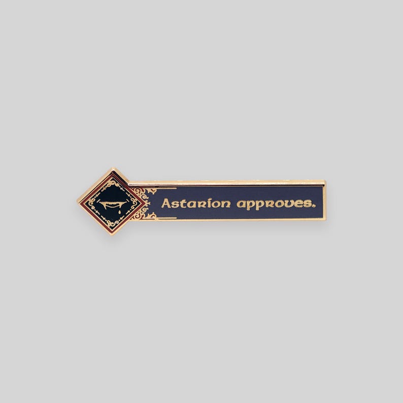 May include: Gold-colored enamel pin with a dark blue background and gold lettering. The pin features a stylized image of a coffin with a crown and the text "Astarion approves."