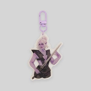 May include: Purple and white keychain featuring a character holding a sword. The character has purple skin, long white hair, and is wearing a black and silver outfit.