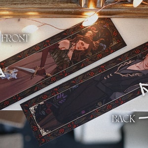 May include: Two bookmark designs with gold accents and a dark background. The front features a woman with long red hair holding a sword. The back features a person with dark hair wearing a black jacket. Both bookmarks have a red berry and leaf border.