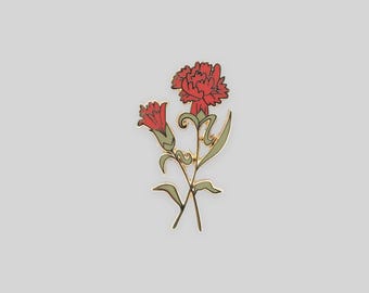 May include: A gold-toned metal enamel pin featuring two red carnation flowers with green stems and leaves. The design displays one fully bloomed flower and one smaller bud, both rendered with clean lines and vibrant red and olive green enamel fill.