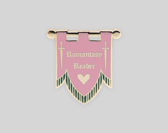 May include: A gold-toned metal enamel pin shaped like a banner. The pin features a pink background with the text "Romantasy Reader" in a white gothic font, flanked by two white swords, a white heart, and dark green vertical stripes at the base.
