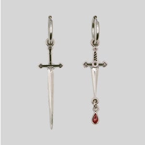 May include: A pair of silver hoop earrings with a sword pendant. One earring has a red gemstone drop.