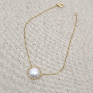 Peut inclure: Un bracelet en chaîne dorée avec un pendentif en forme de grosse perle blanche.