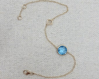 May include: A delicate gold chain bracelet with a round blue gemstone and a small diamond-shaped pendant.