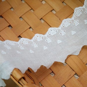 Peut inclure: Bordure en dentelle de coton blanche avec un bord festonn&eacute; et de petites fleurs brod&eacute;es. La dentelle est pr&eacute;sent&eacute;e sur un panier tiss&eacute;.