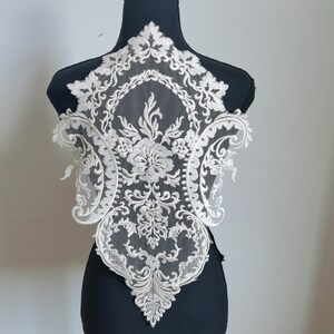 May include: White lace applique with a floral design. The lace is delicate and intricate, with a scalloped edge.