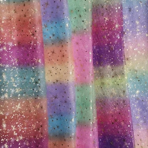 Könnte beinhalten: Mehrfarbiger, durchsichtiger Stoff mit einem Regenbogen-Ombre-Effekt und silbernen Glitzersternen. Der Stoff ist aus einem weichen, leichten Material gefertigt und hat einen zarten, ätherischen Look.