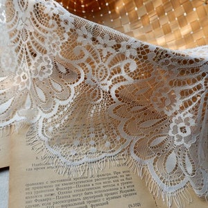 May include: White lace trim with a delicate floral pattern. The lace has a scalloped edge and a frayed finish.
