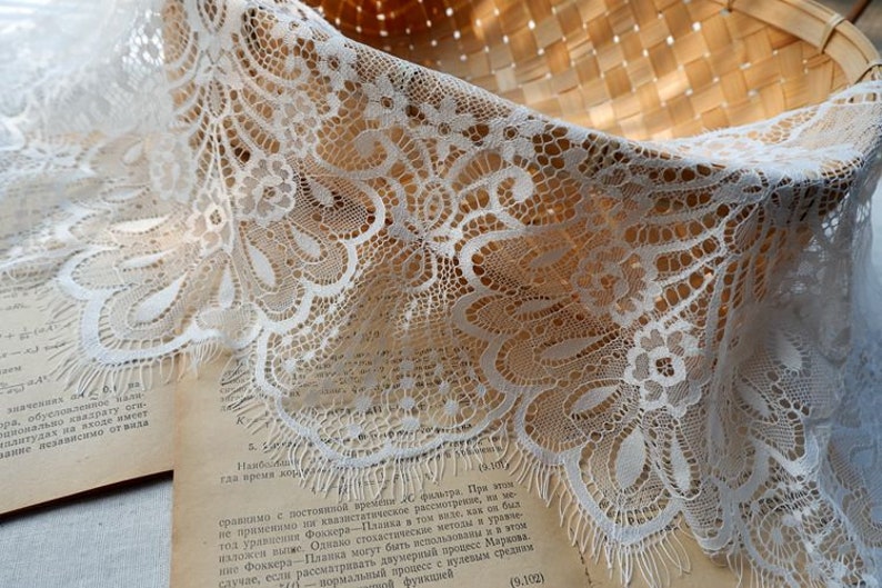May include: White lace trim with a delicate floral pattern. The lace has a scalloped edge and a frayed finish.